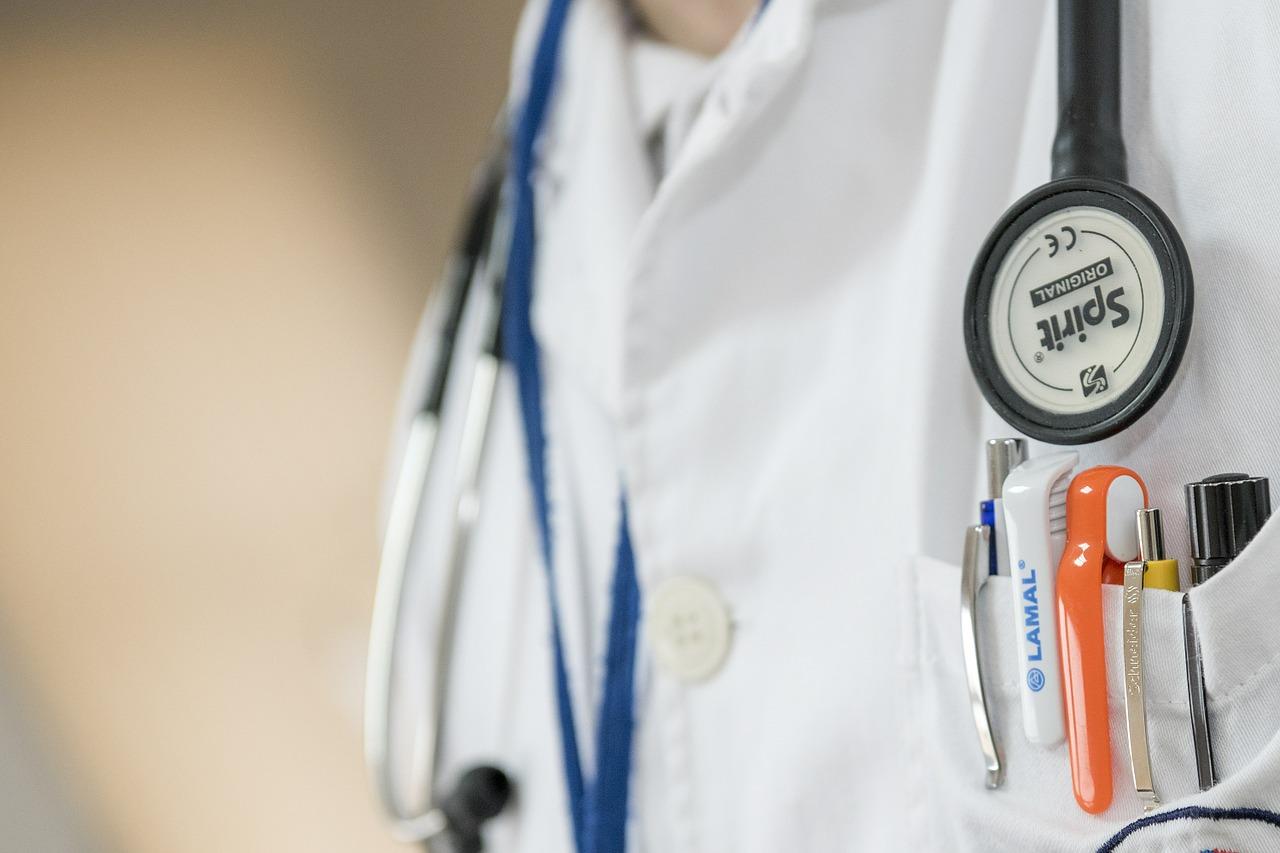 A doctor 's coat and stethoscope hanging on the side of his uniform.