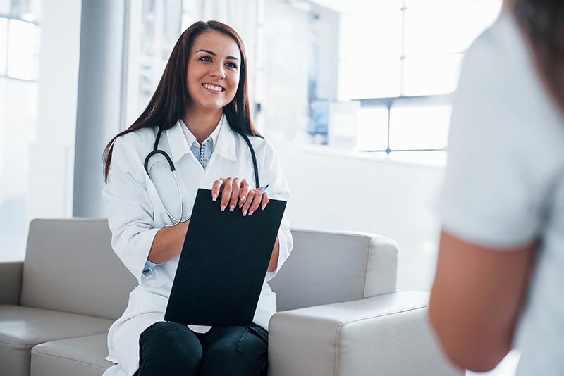 A woman in white coat holding black folder.