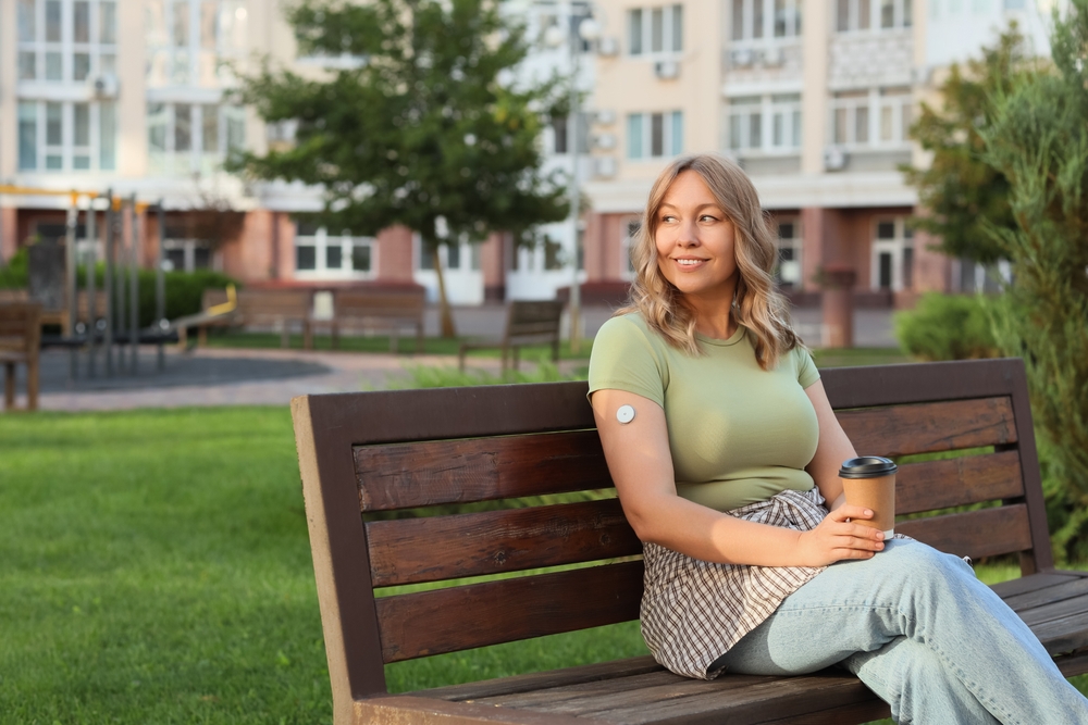 Diabetic woman with glucose sensor and coffee cup sitting on bench outdoors