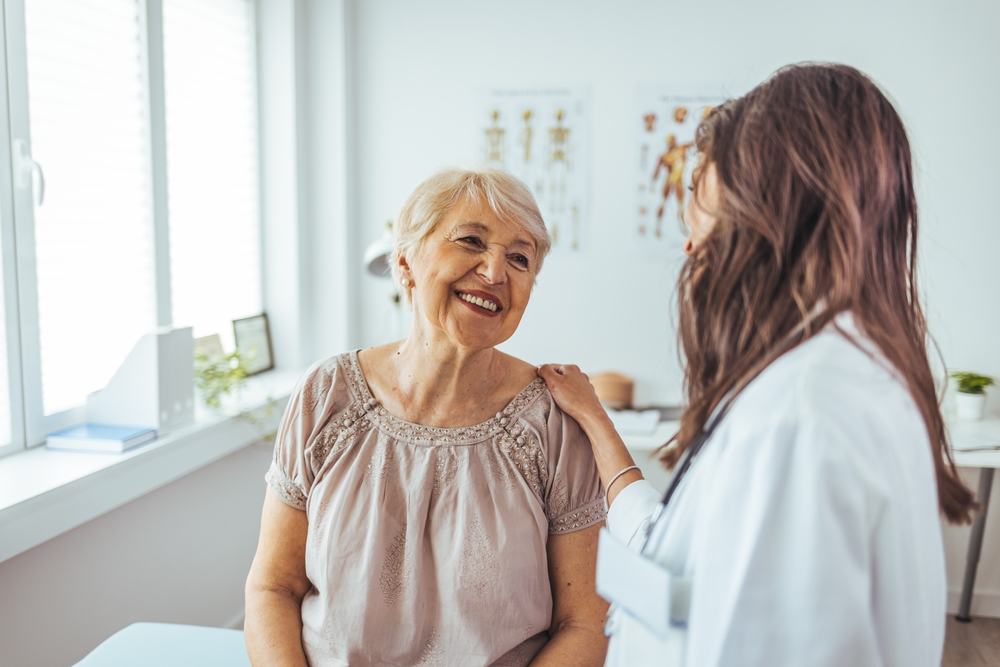 A cheerful senior woman engaging with her caring doctor during a consultation in a modern, bright medical office. Warm interaction showcasing trust and healthcare professionalism