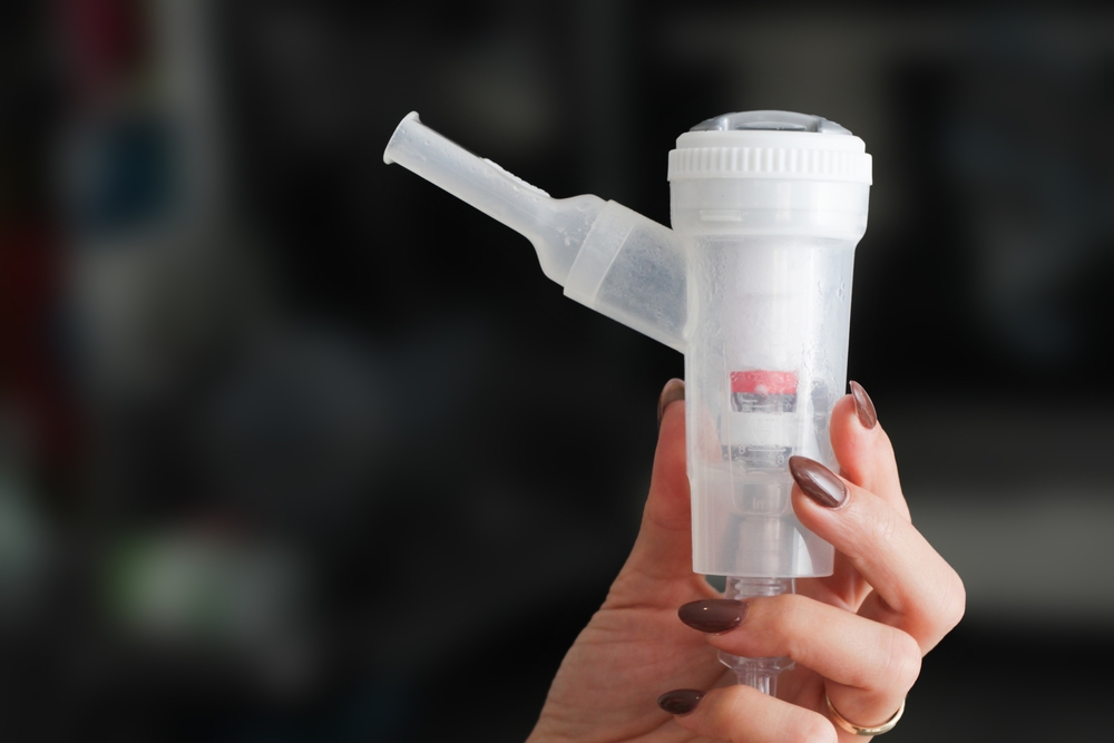 Nebulizer in hand background. Nebulizer isolated. Medical device background. Woman hand holding nebulizer. Lungs and throat treatment. Mouth inhaler.