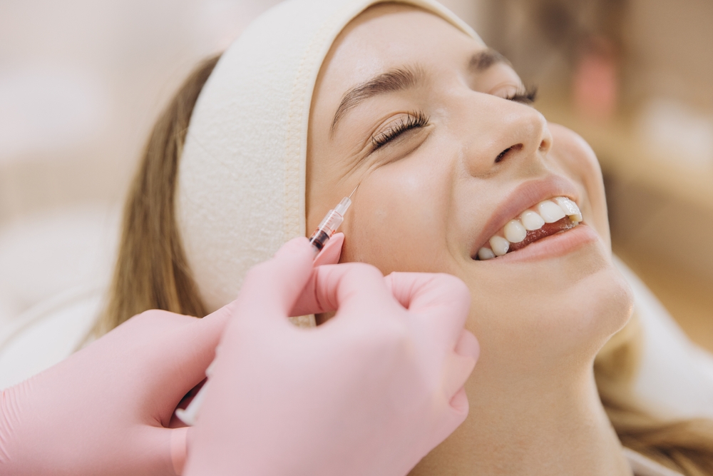 Professional beautician performing botox injection, treating wrinkles on smiling female client’s skin during cosmetic procedure